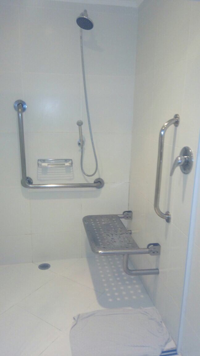Descrição da imagem para cego ver: espaço para banho adaptado com assento dobrável e adequação na altura do chuveiro.